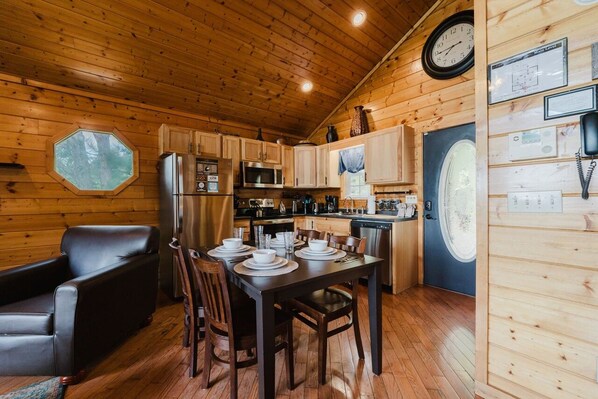 A wooden cabin interior with a dining table set for four, a refrigerator, a microwave, and wooden cabinets.