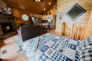 Interior acogedor de una cabaña con chimenea, una cama con colcha, zona de comedor y cocina.