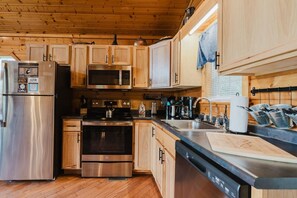 A modern kitchen with stainless steel appliances, wooden cabinets, and a black countertop.