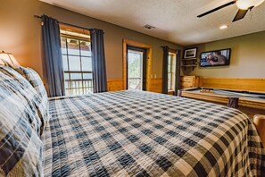 Un dormitorio con una cama grande, televisión, mesa de billar y ventana con cortinas.