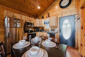 A wooden cabin interior with a dining table set for four, a refrigerator, microwave, and a sink.