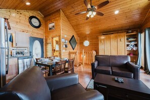 A cozy cabin interior with a dining area, a living room with a sofa, and a kitchen with modern appliances.