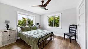 A bedroom with a bed, nightstands, a chair, a ceiling fan, and windows with a view of greenery. - Beautiful Villa With First Class Amenities on Charlotte Harbor, Orlando Villa 5584 (Punta Gorda)