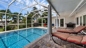A covered outdoor swimming pool with lounge chairs, a barbecue area, and a view of palm trees and a boat. - Beautiful Villa With First Class Amenities on Charlotte Harbor, Orlando Villa 5584 (Punta Gorda)