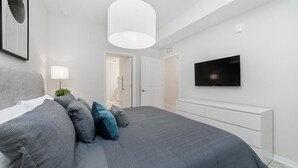 Quarto moderno com uma cama grande, televisão de tela plana na parede e um console branco.