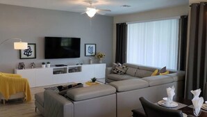 Ein modernes Wohnzimmer mit grauem Sofa, einer weißen Unterhaltungsecke und einem Deckenventilator.