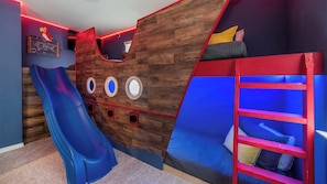 A playroom with a slide, climbing wall, and bunk beds.