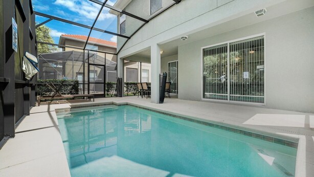 Piscina interior com paredes de vidro transparente, área de estar com espreguiçadeiras e vista para os edifícios ao redor.