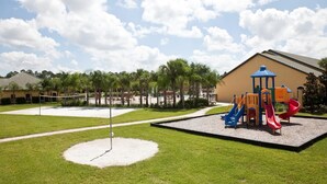 A playground with slides and a small pavilion, surrounded by a well-maintained lawn and a building in the background. - Charming Townhome Sleeps 8 5577 (Kissimmee)