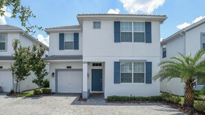 A two-story residential building with a white exterior and blue shutters, a garage door, and a small front porch. - Rent This Luxury 5 Star Villa on Storey Lake, Orlando Villa 5482 (Kissimmee)