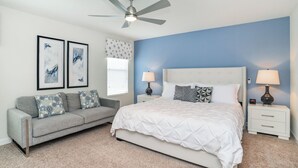 A bedroom with a bed, a grey sofa, two bedside tables with lamps, and framed artwork on the wall. - Rent This Luxury 5 Star Villa on Storey Lake, Orlando Villa 5482 (Kissimmee)