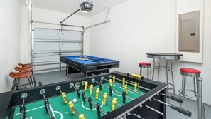 Una habitación con mesa de futbolín, mesa de billar y barra con taburetes.