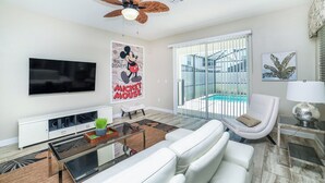 A modern living room with a flat-screen TV, a white sofa, a coffee table, and a ceiling fan. - Rent This Luxury 5 Star Villa on Storey Lake, Orlando Villa 5482 (Kissimmee)