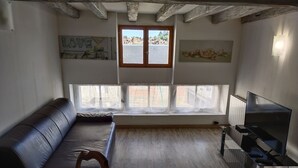 A cozy living room with a leather sofa, a TV, and a window with curtains. - House on the Loire (Gien)