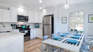 A modern kitchen with white cabinets, stainless steel appliances, and a dining area with blue plates and metal chairs.