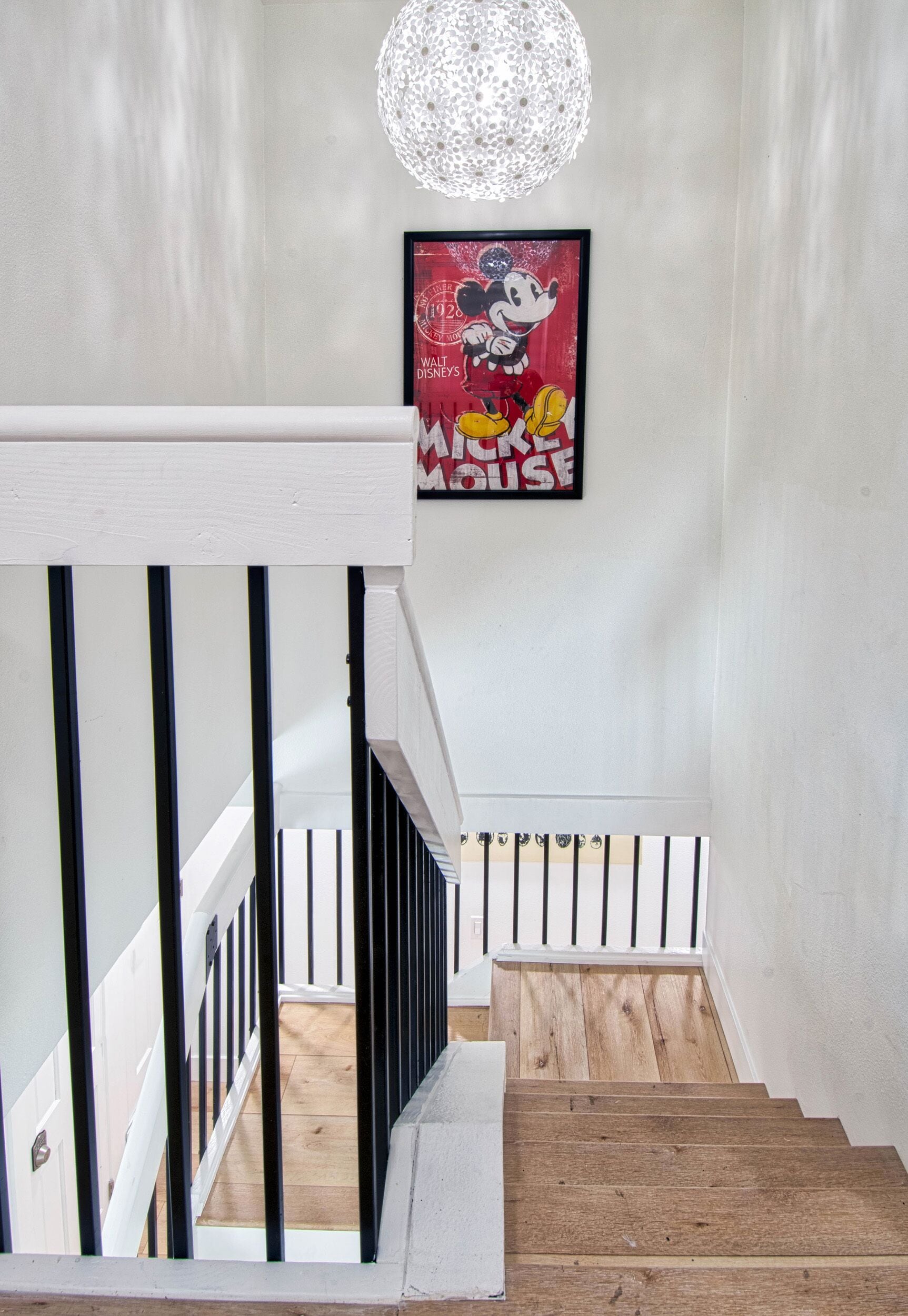 Een trap met houten treden en zwarte leuningen, die uitkomt op een plateau met een lijstfoto van Mickey Mouse.