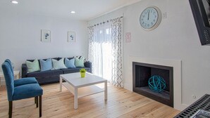 A living room with a sofa, a coffee table, a blue chair, a fireplace, and a clock on the wall.