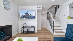 A modern living room with a flat-screen TV, a fireplace, a staircase, and a blue sofa.