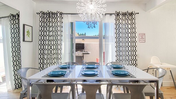 A dining area with a table set for six, a chandelier, and a view of the outdoors.