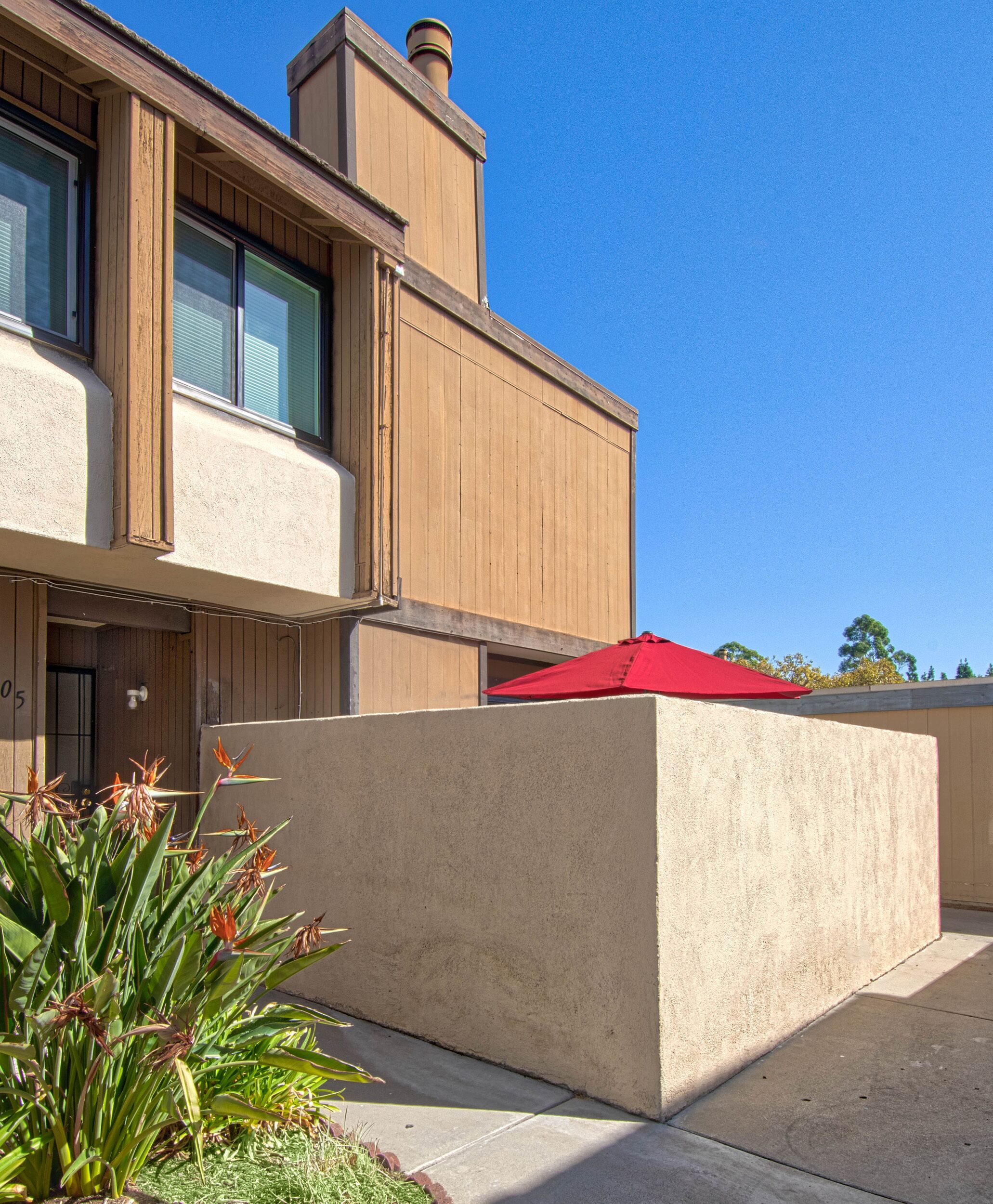 A modern building with a beige facade, a red umbrella, and a small garden area with plants.
