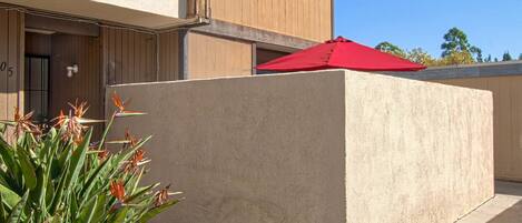 A modern building with a beige facade, a red umbrella, and a small garden area with plants.