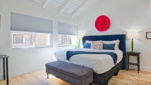A bedroom with a large bed, a bench, two windows, a red decorative item, and a green lamp.