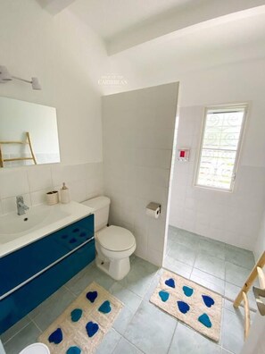 A bathroom with a white sink, blue cabinet, white toilet, and a shower area.