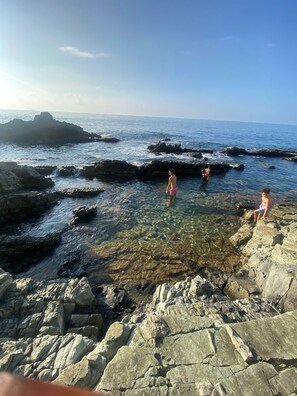 A rocky coastal area with clear water and a view of the sea.