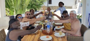 A group of people toasting at a wooden table with various drinks and plates of food.