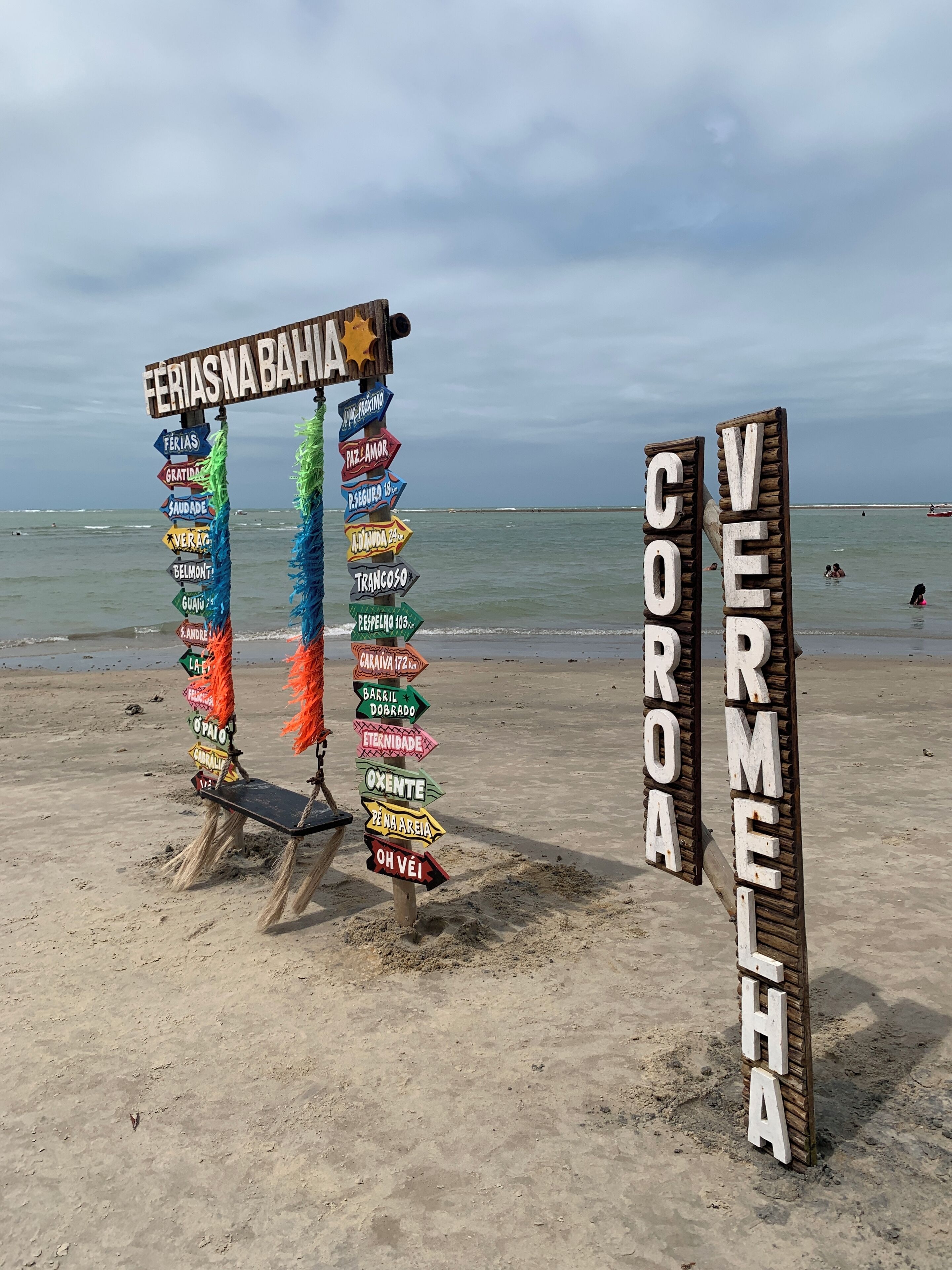 Un cartel de playa con varias flechas direccionales y un letrero de madera que dice 'VERMEIA COROA'.