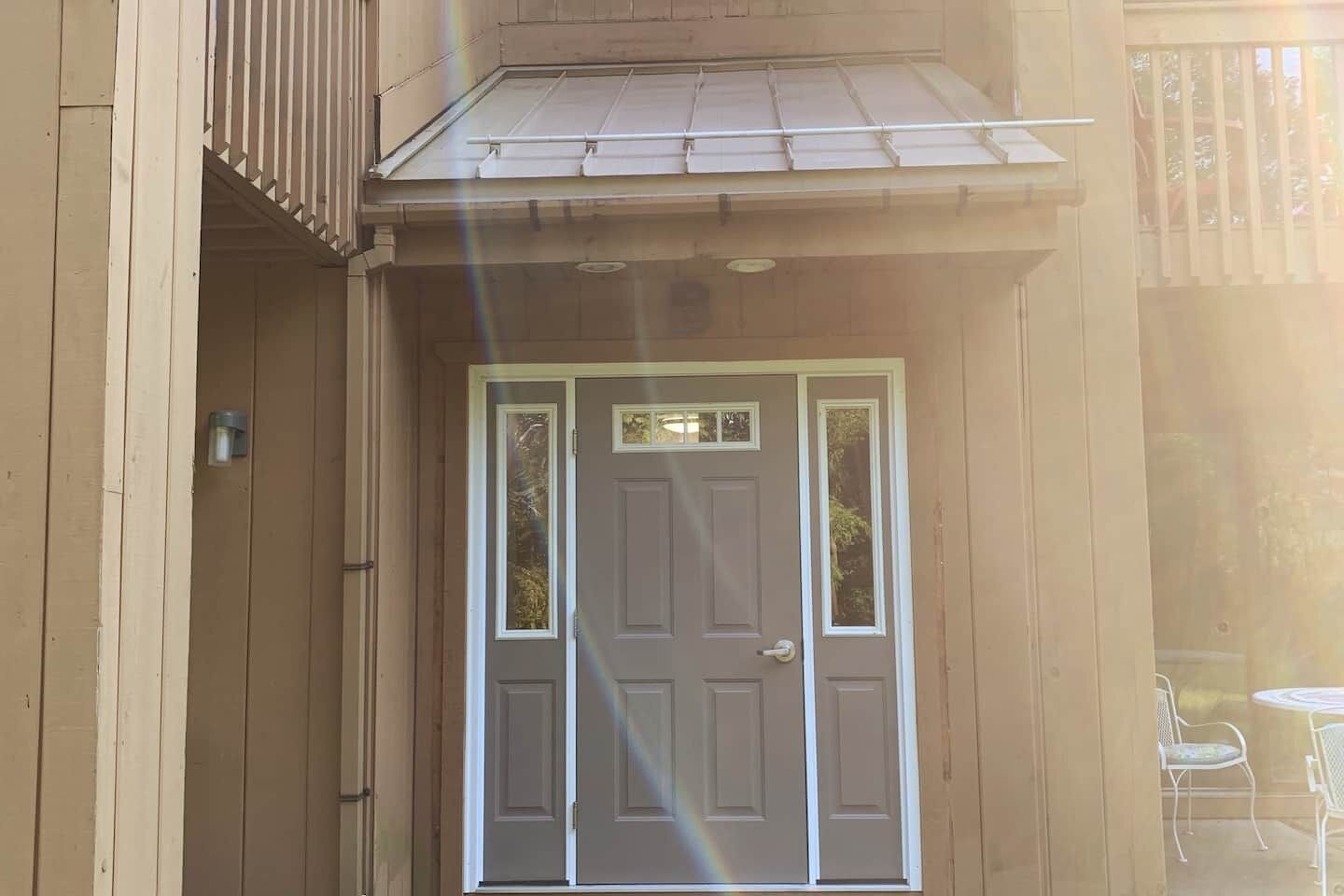 A wooden door with a small window, a balcony with a metal railing, and a small table with chairs outside.