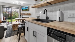 A modern kitchen with a wooden countertop, black sink, and white tiled backsplash. - Hillside Getaway Ski-In Ski-Out Retreat in Ellicottville, NY Sleeps 4 (Ellicottville)