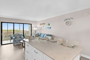 Et moderne køkken med en stor ø, et spiseområde med et hvidt bord og stole, samt en balkon med udsigt.