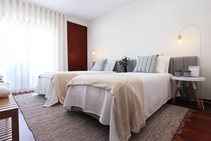 Hotellihuone, jossa on kaksi sänkyä, yöpöytä lampun kanssa, pieni kasvi ja näkymä ulos.