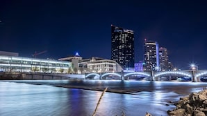 A nighttime cityscape with a river, a bridge, and modern buildings. - Finnley Boutique King Room (Grand Rapids)