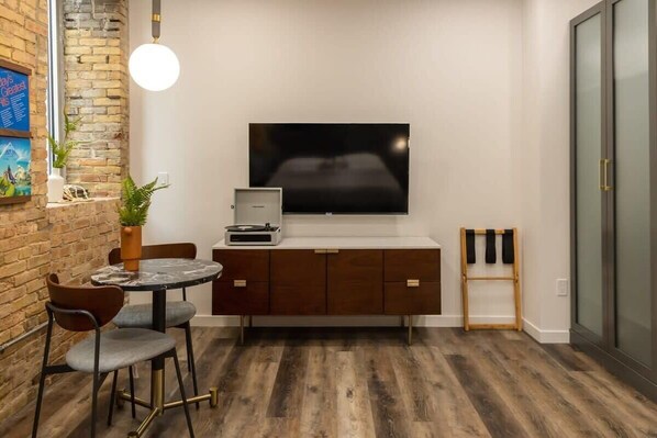 A modern room with a TV, a small table with chairs, a cabinet, and a wooden floor.