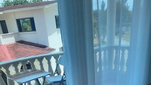 A balcony with a table and chairs, a sofa, and a view of a building with a tiled roof. - Best west $ (Kiambu County)