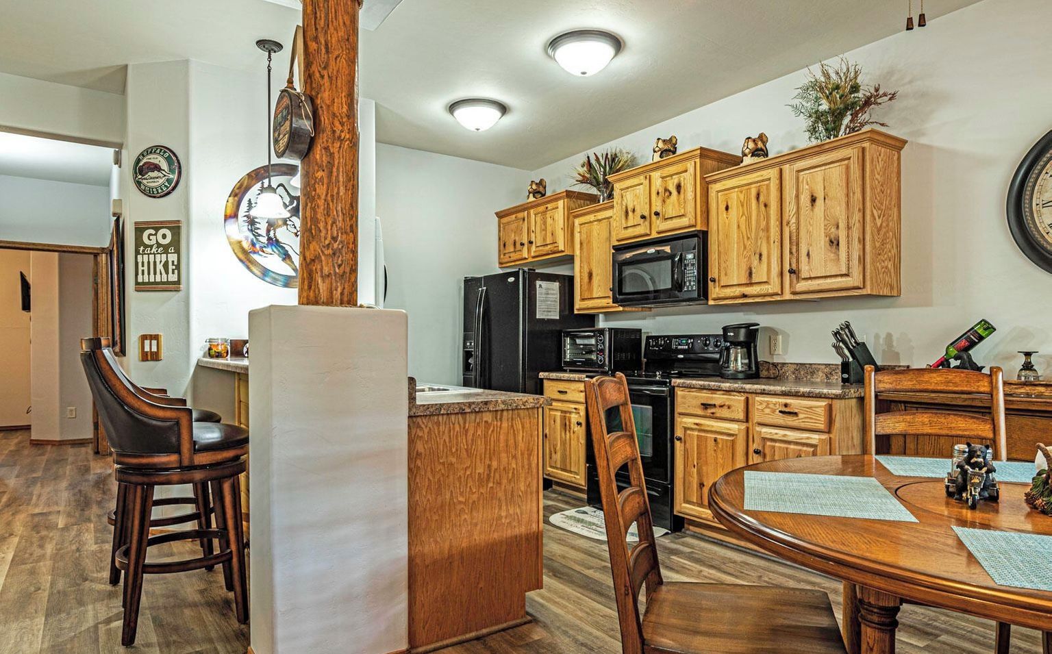 Una cocina con armarios de madera, un refrigerador, un microondas y un comedor con mesa y sillas.