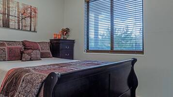 A bedroom with a bed, a dresser, a window with blinds, and a painting on the wall.