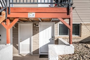 Une entrée d’immeuble avec un panneau d’avertissement indiquant une faible hauteur sous plafond, une porte blanche et une petite fenêtre.