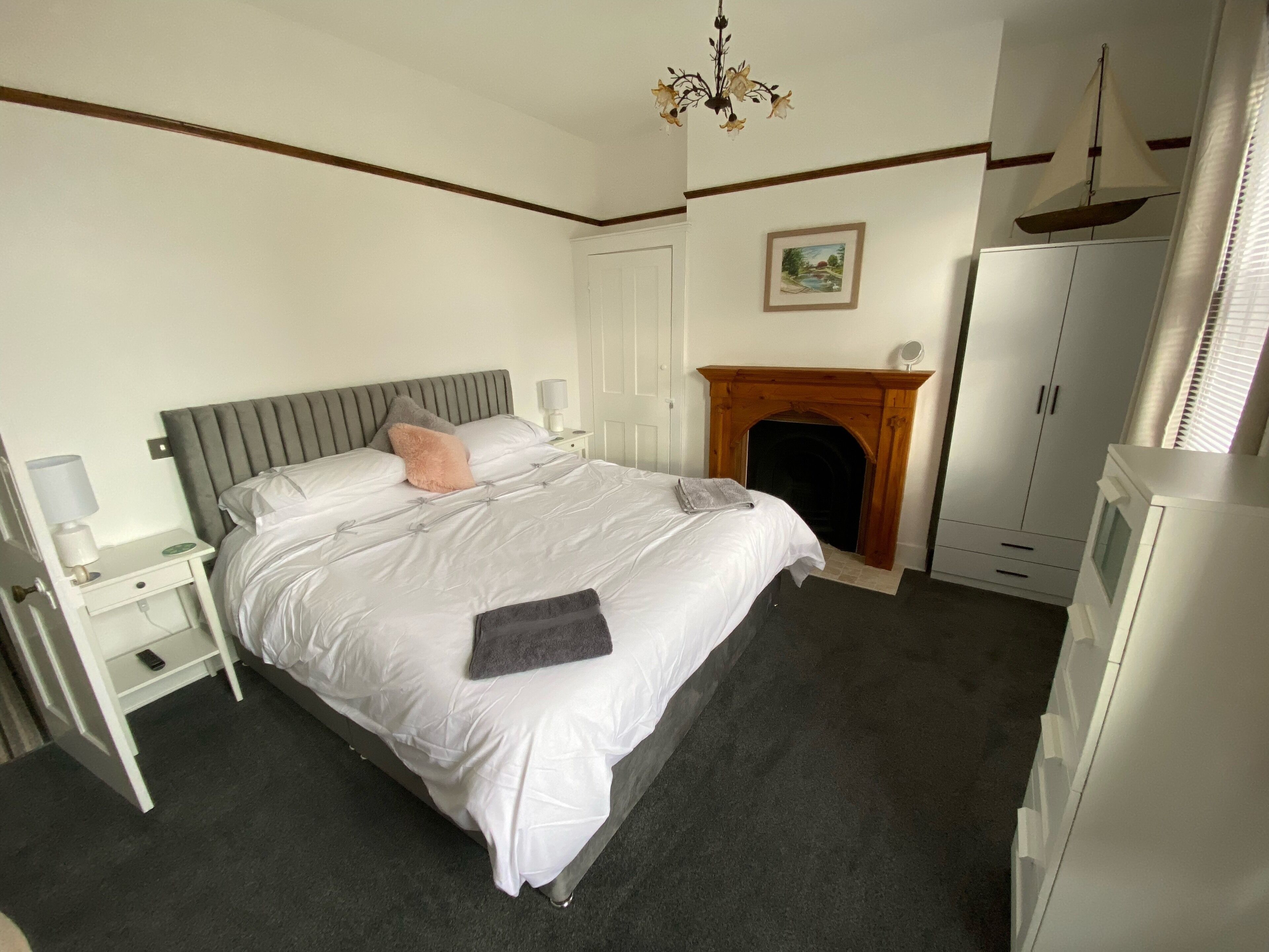 A neatly arranged bedroom with a bed, bedside tables, a fireplace, and a wardrobe.