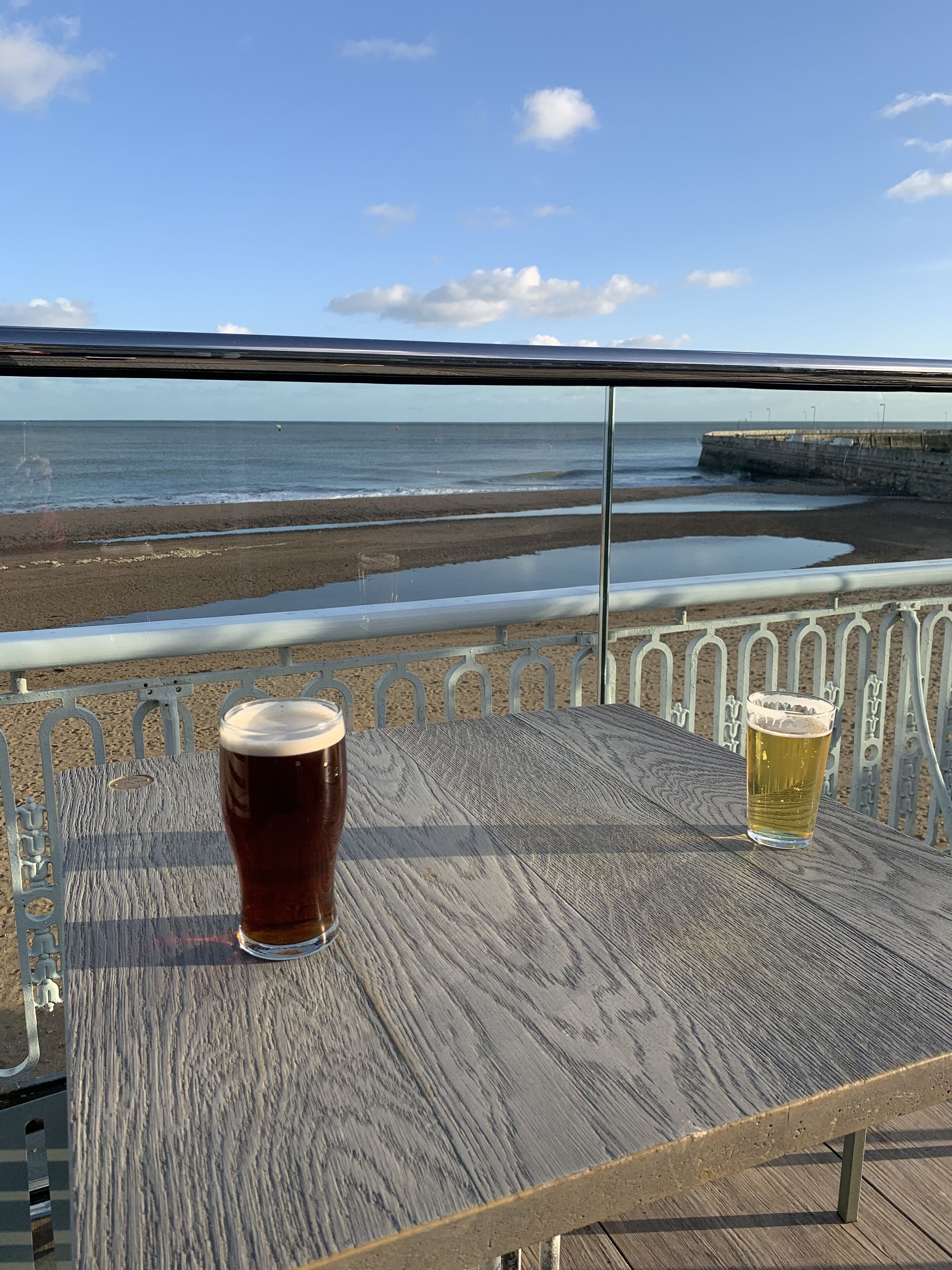 Ein Holztisch mit zwei Biergläsern, mit Blick auf Strand und Meer.