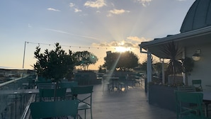 Ein Sitzbereich im Freien mit Tischen und Stühlen, ein klarer Himmel und ein Sonnenuntergang im Hintergrund.
