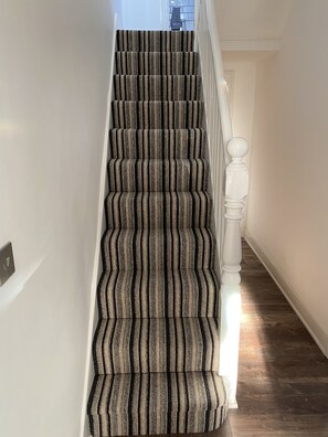 Una escalera con alfombra a rayas y barandilla blanca.