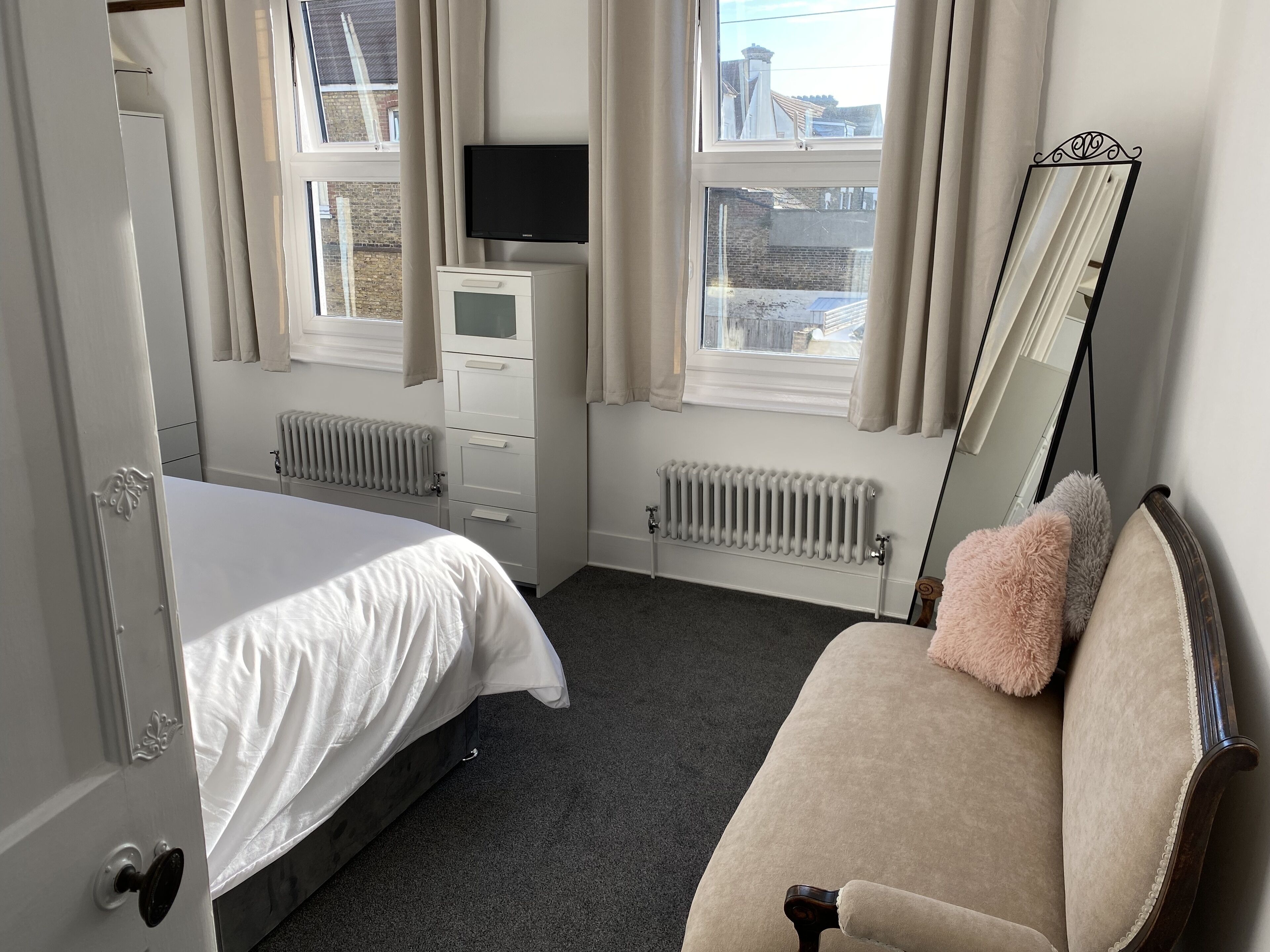 A bedroom with a bed, a dresser, a TV, a radiator, and a mirror.