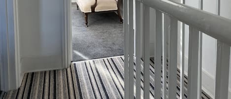 A hallway with a striped carpet leading to a bedroom.