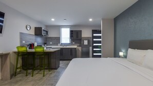 A compact hotel room with a kitchenette, a bed, and a dining area.
