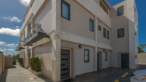 A multi-story residential building with a flat facade, multiple windows, and a car parked in the driveway.