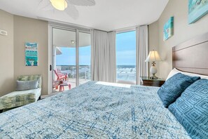 Een hotelkamer met een groot bed, een balkon met uitzicht, een stoel en een nachtkastje met een lamp.