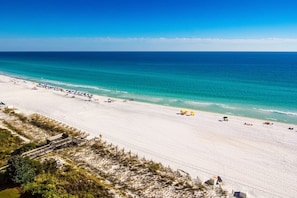 Een uitgestrekt strand met helderblauw water, een zandstrand en enkele parasols.